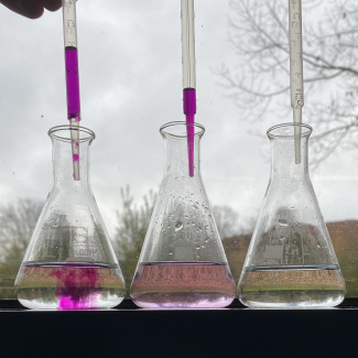 Bild aus dem Chemischen Fotokalender: Drei Erlenmeyerkolben, in die eine lilafarbene Flüssigkeit getropft wird