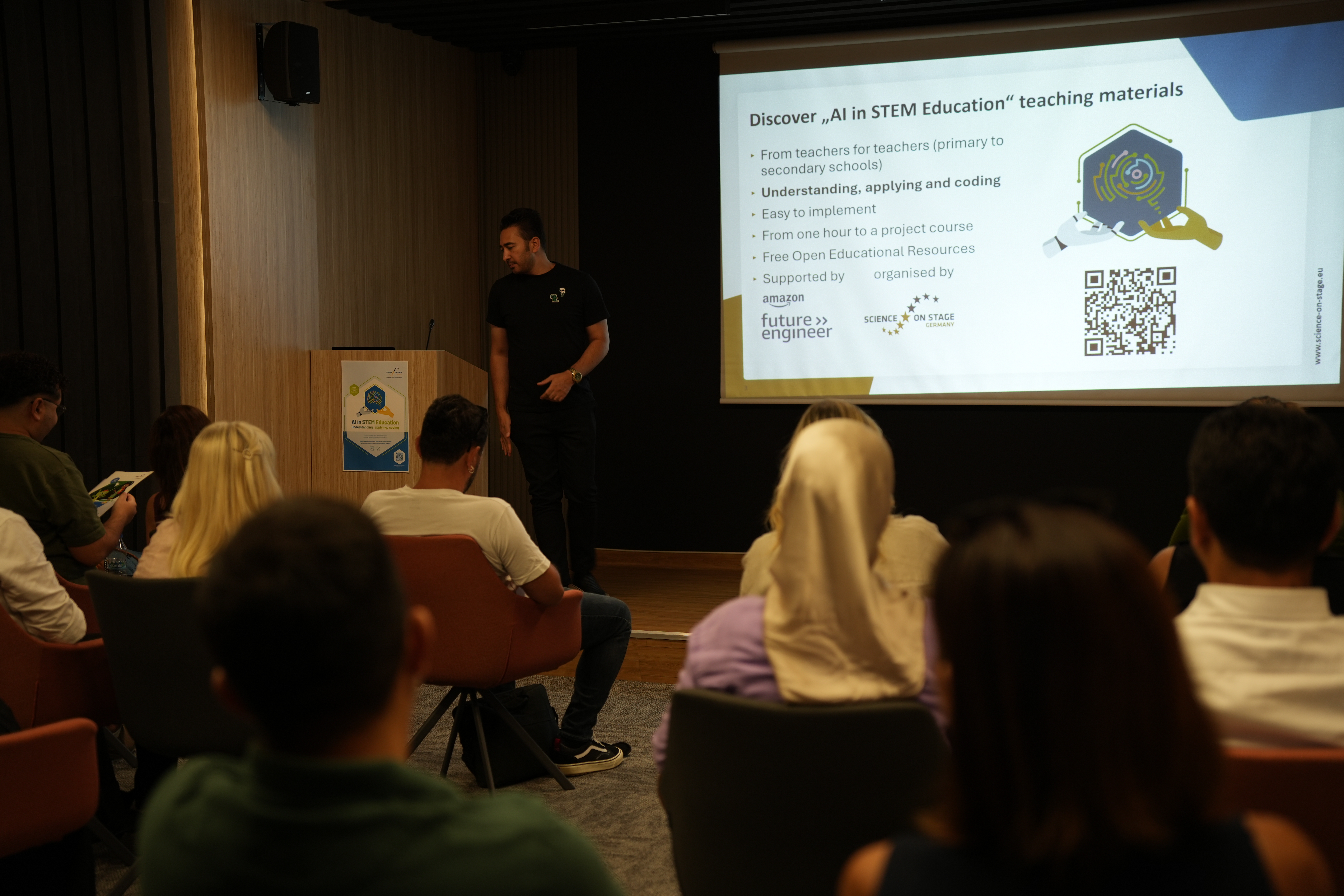 Blick von hinten auf Seminarteilnehmer vor einer Leinwand, daneben ein Referent am Pult