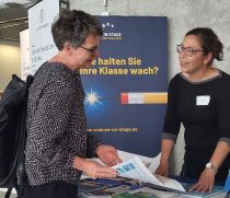 Zwei Frauen im Gespräch an einem Stand vor dem Banner "Wie halten Sie Ihre Klasse wach?"