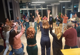 28 Personen stehen in einem Kreis und heben ihre Arme.