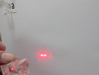 Richtet man den Laserstrahl auf den Kalkspat-Kristall, erscheinen hinter dem Kristall zwei Laserstrahlen.