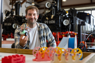 Ein Aussteller mit Objekten seines Messestands vor zwei Güterlokomotiven