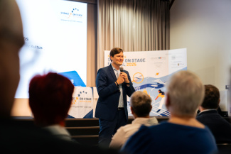 Ein Redner vor Publikum, über die Köpfe der Zuschauer hinweg gesehen