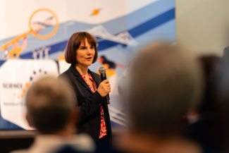 Eine Rednerin mit Mikrofon, über die Köpfe des Publikums hinweg gesehen