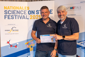 Zwei Männer mit Gewinnerurkunde vor der Sponsorenwand des Science on Stage Festivals