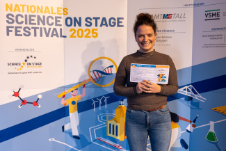 Eine Frau mit Gewinnerurkunde vor der Sponsorenwand des Science on Stage Festivals