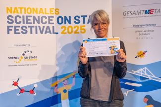 Eine Frau mit Gewinnerurkunde vor der Sponsorenwand des Science on Stage Festivals