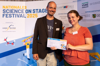 Eine Frau und ein Mann mit Gewinnerurkunde vor der Sponsorenwand des Science on Stage Festivals