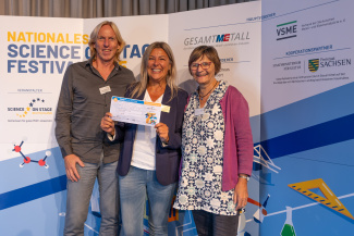 iEin Man und zwei Frauen mit Gewinnerurkunde vor der Sponsorenwand des Science on Stage Festivals