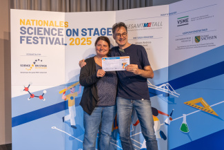 Eine Frau und ein Mann mit Gewinnerurkunde vor der Sponsorenwand des Science on Stage Festivals