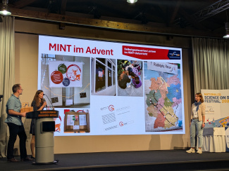 Zwei Personen vor einer Leinwand mit einer Bildercollage zu "MINT im Advent"