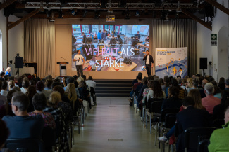 Zwei Personen vor einer Leinwand mit der Titeleinblendung "Vielfalt als Stärke"