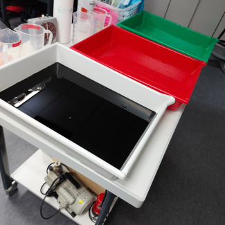 eine weiße, einerote und eine grüne Wanne liegen auf dem Tisch, die weiße Wanne ist mit schwarzer Flüssigkeit gefüllt