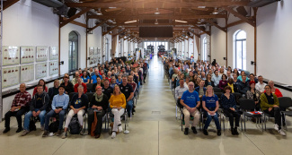 Ein voll besetzter Veranstaltungssaal, im Hintergrund zwei Dampflokomotiven