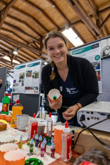 Eine Ausstellerin an einem Messestand mit einem wissenschaftlichen Farbexperiment