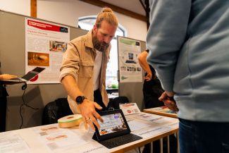 Ein Austeller zeigt einem Besucher an einem Messestand etwas auf einem Tablet