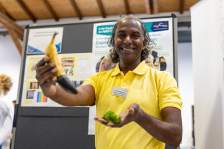 Eine Person in gelbem T-Shirt hält an einem Messestand eine Banane in die Höhe
