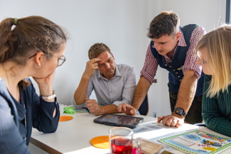 Vier Personen beugen sich bei einem Workshop über ein Tablet